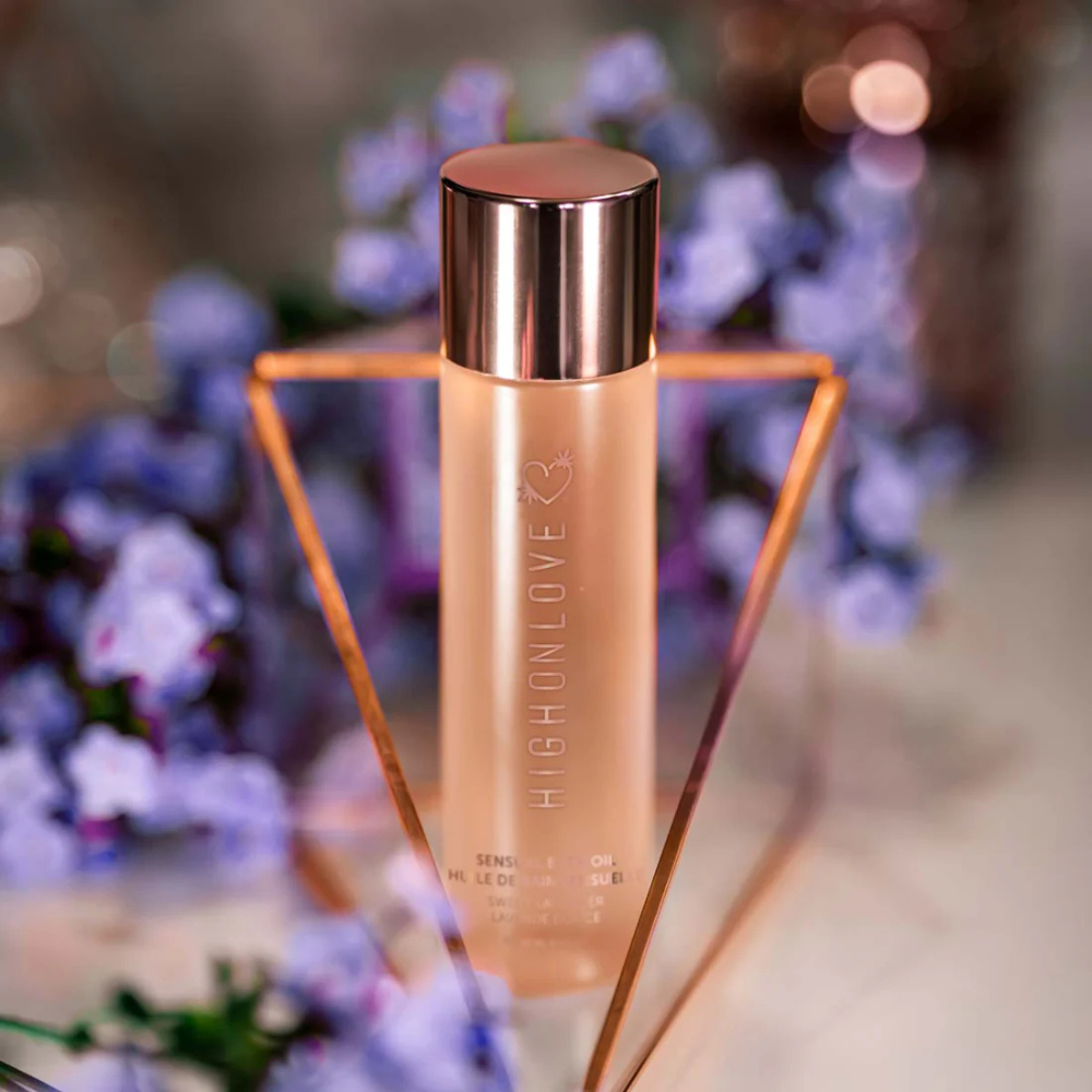 A gold bottle of Sweet Lavender Sensual Bath Oil by High On Love sitting by lavender.