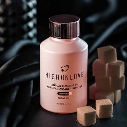 A pink bottle of Sugar High Massage Oil by High On Love next to cubes of sugar against a dark background.
