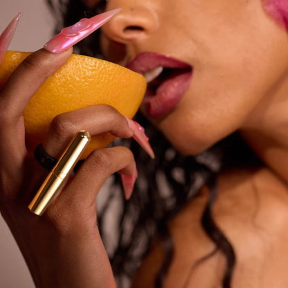 A lady wearing the 24k Gold Vibrator  Ring from the Tease Collection eating an orange.