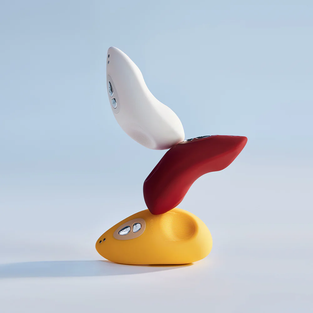 A red, white and yellow Tremble clitoral vibrator by Liberator piled on top of each other against a white background.