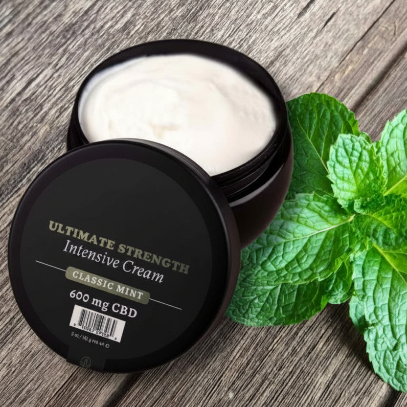 A black bottle Classic Mint of Ultimate Strength Intensive muscle cream sitting next to a mint leaf.
