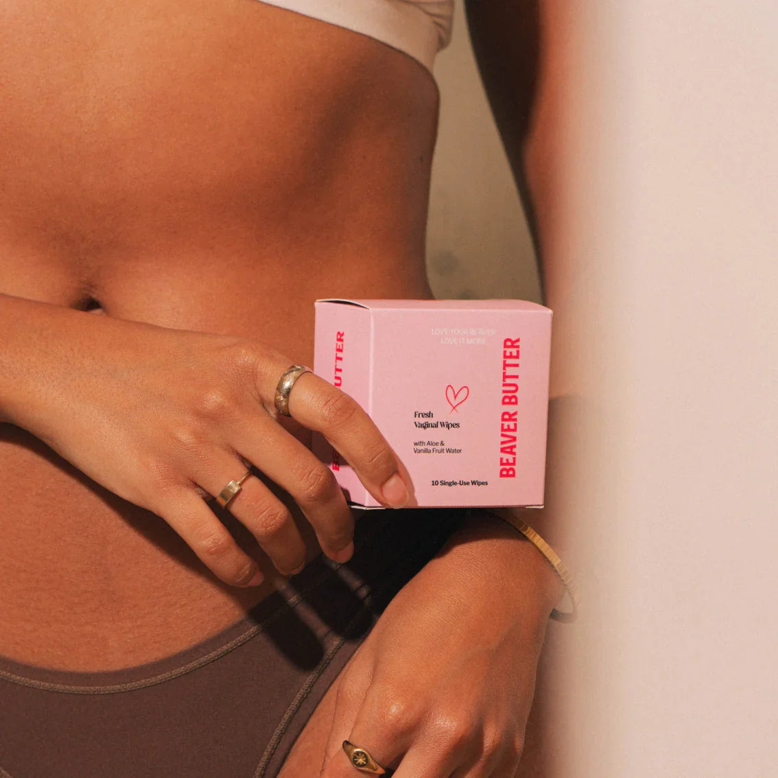 A lady holding pink box of Beaver Butter Fresh Vaginal Wipes by ECN in the pelvic region.