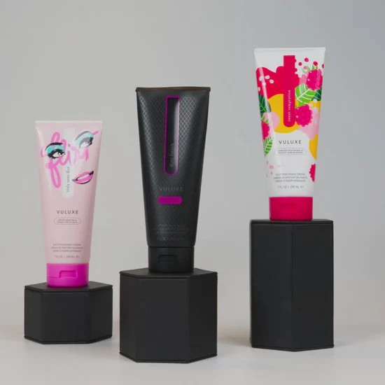 Three Vuluxe shave cream products on black stands with a gray background