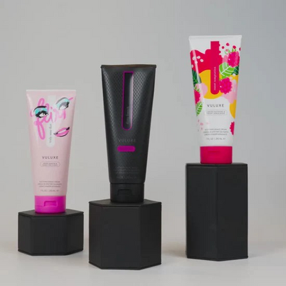Three Vuluxe shave cream products on black stands with a gray background