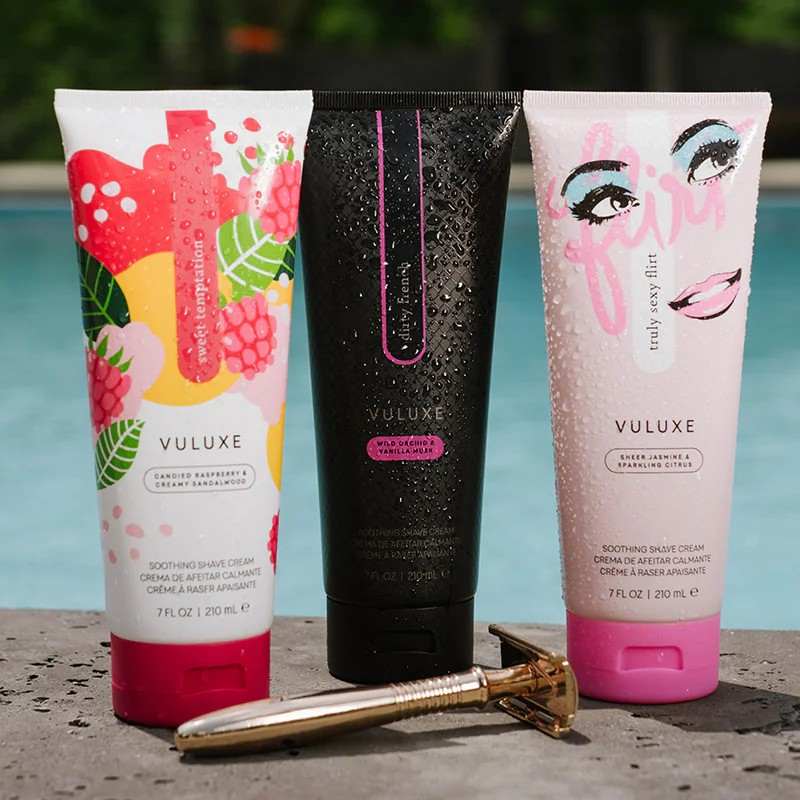 Three Vuluxe shave cream bottles with colorful packaging by a pool.