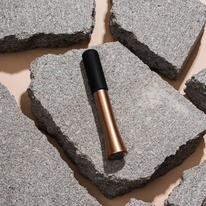A Wink discreet vibrator in rose gold with the black silicone cap on it sitting on some rocks.