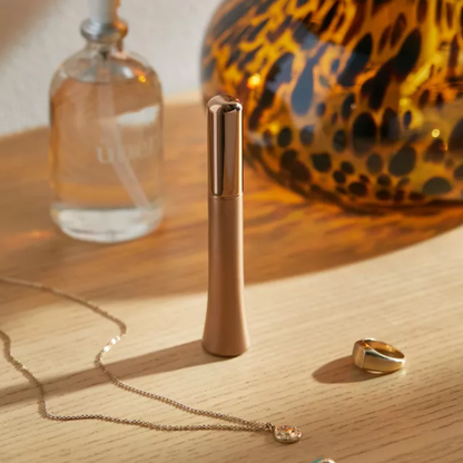 A Wink discreet vibrator in rose gold sitting on a table next to a necklace and ring.