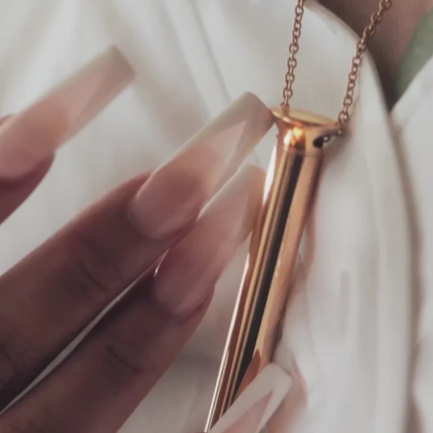 Rose gold necklace held by a hand with light nail polish on a white background